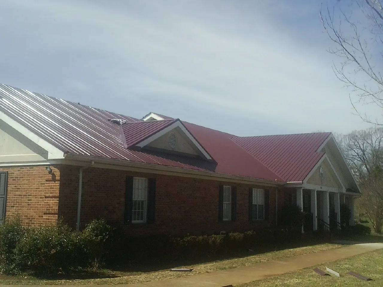 Red metal roof with gabled entries on a long brick building, from a Hail Damage Roof Repair job in Tatums