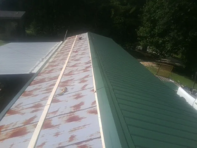 Old rusted panels beside newly installed green metal roofing — Wind Damage Roof Repair by Roofing Brothers in Tatums