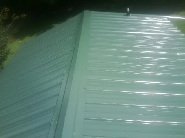 New green metal panels meeting at the ridge of a roof — Flat Roof Repair work by our crew in Tatums