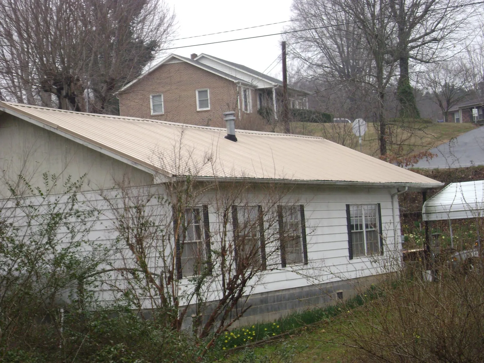 Tan metal roof on a white sided house set into a hillside — Commercial Roofing by Roofing Brothers in Tatums