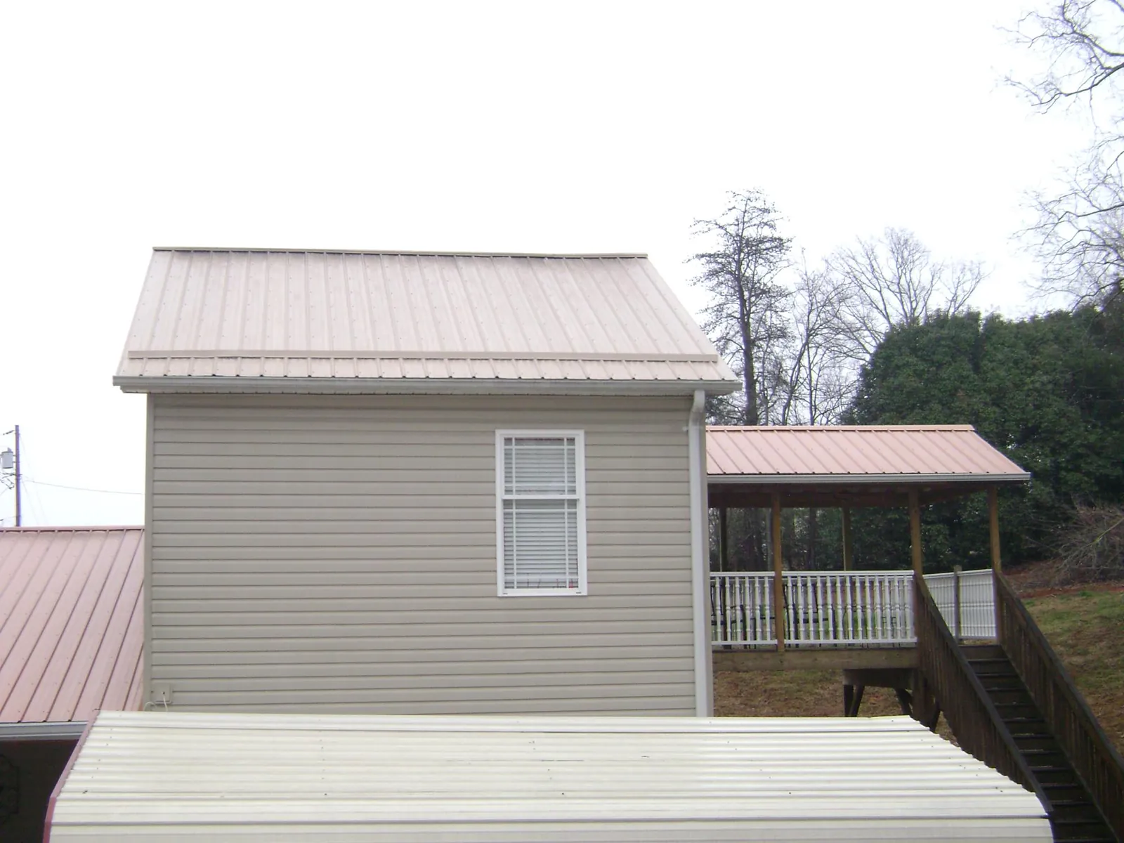 Tan metal roofs on a two story addition and attached porch, from a Roof Replacement job in Tatums
